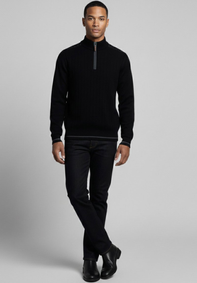 Suéter negro acanalado con cremallera y cuello alto, combinado con vaqueros oscuros y botas negras, con un sutil ribete de contraste en el cuello.