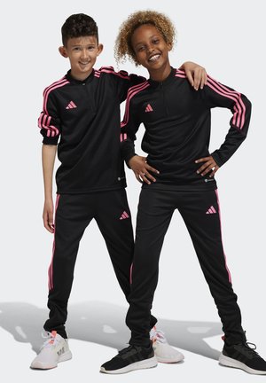 Schwarze sportliche Trainingsanzüge mit pinken Streifen, mit Reißverschlusskragen, weicher Textur, mit dem Adidas-Logo auf der Brust und den Hosen, getragen von zwei Kindern.