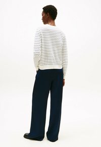 Maglione a righe blu e bianche con una vestibilità rilassata, abbinato a pantaloni larghi blu realizzati in un tessuto leggero e liscio.