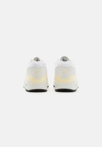 Vita och ljusgula Nike Air-sneakers med en slät ovandel, vadderad krage och svart gummisula. Har logotyp på hälen och tungan.