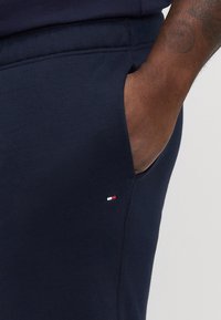 Granatowe dresy wykonane z miękkiego materiału, z boczną kieszenią i małą łatką z logo w kolorach czerwonym, białym i niebieskim w pobliżu szwu kieszeni.