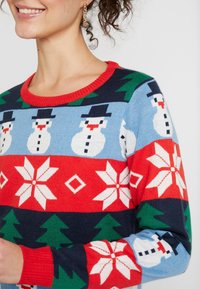 Stickad tröja med snögubbe och blommönster i blått, rött, grönt och vitt. Rund röd krage och långa ärmar. Strukturerad tyg.