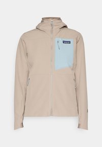 Vaaleanbeige vetoketjullinen takki hupulla, sininen rintatasku Patagonia-logolla ja kaksi sivuvetoketjutaskua.