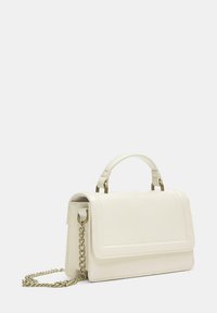 Bela usnjena torbica z izrazito obliko, zgornjim ročajem in zlato verižico. Ima sprednjo preklopno zaponko in minimalistične podrobnosti šivov.