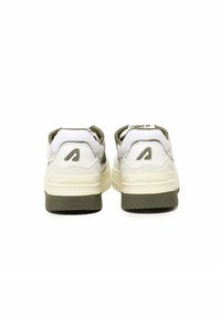 Un paio di sneakers bianche e beige con suole verde scuro, viste da dietro su sfondo bianco.