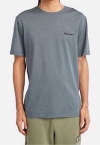 T-shirt gris à manches courtes en coton, doté d'un col rond et du logo Timberland imprimé en noir sur le côté gauche de la poitrine.