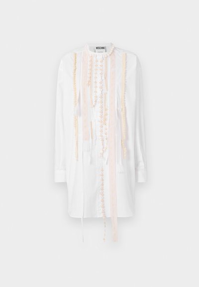 Biela košeľa s detailným broskyňovým vyšívaním a kaskádovými ozdobami, dlhými rukávmi a uvoľneným strihom.