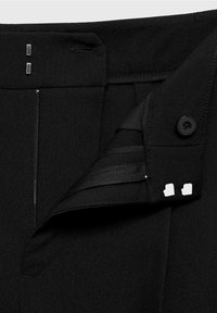 Pantalon noir avec une fermeture éclair, deux fermoirs carrés métalliques et un bouton. Le tissu semble lisse avec une coupe ajustée.