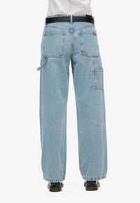 Pantalones cargo de denim azul claro con un ajuste relajado, cinco bolsillos y un cinturón negro, con costuras visibles y diseño de pierna recta.
