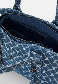Sac à main en tissu bleu à motifs avec fermeture éclair métallique et clous, ouvert pour montrer l'intérieur bleu foncé et l’étiquette interne.