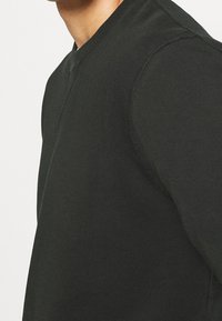 Černý bavlněný mikina s kulatým výstřihem a bezešvým designem, obsahující žebrované detaily na límci a manžetách. Hladká textura, obepínající tvar.