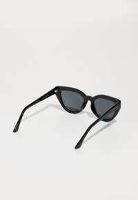 Óculos de sol pretos em formato de olho de gato com lentes escuras, acabamento brilhante, hastes largas e detalhes de marcação em dourado nos lados.