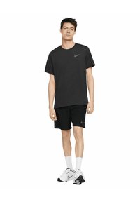 T-shirt nera in cotone con logo Nike grigio, abbinata a pantaloni corti neri con un piccolo logo. Il modello indossa calzini bianchi e sneakers bianche.