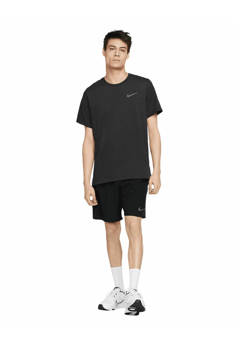 T-shirt nera in cotone con logo Nike grigio, abbinata a pantaloni corti neri con un piccolo logo. Il modello indossa calzini bianchi e sneakers bianche.