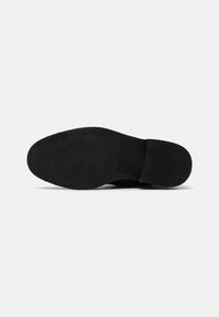 Suela de zapato negra con una textura suave, que presenta un patrón acanalado para mayor tracción y una ligera curvatura hacia la zona de los dedos.