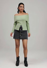 Light green, off-the-shoulder knit top with a ribbed texture and button detail, paired with a black denim skirt featuring gold buttons. Black ankle boots.
