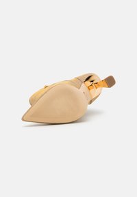Zapato de tacón de ante sintético dorado con punta afilada, suela lisa y acento metálico en el tacón. Material texturizado con un sutil brillo.