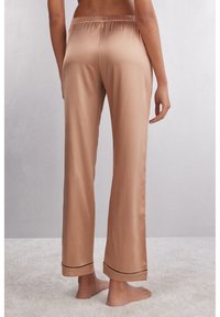 Satijnen pyjamabroek in lichtbeige, met een elastische tailleband en zwarte biezen langs de manchetten. Losse pasvorm met rechte pijpen.