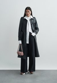 Mustast nahast pikem mantel, valge särk, kõrge vöökohaga tumedad teksad, roosa käekott, valged ja burgundiapunased tossud, minimalistlik disain, sile tekstuur.