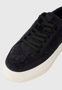 Tenisi din suede negri cu șireturi negre, mici studuri negre care formează modele florale și o talpă groasă din cauciuc alb.