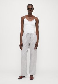 Top con pizzo bianco, pantaloni a righe grigie e bianche con vita elasticizzata e scarpe rosse slip-on. Gli occhiali da sole tondi completano l'outfit.