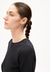 Schwarzes Langarmshirt mit rundem Halsauschnitt, gezeigt an einer Person im Seitenprofil. Die Haare sind zu einem geflochtenen Pferdeschwanz gebunden. Einfaches, sauberes Design.