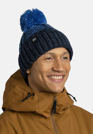 Blaues Pom-Pom-Mütze mit strukturiertem Strickmuster und tiefblauer Farbe. Verfügt über ein kleines schwarzes Buff-Logo an der Seite.