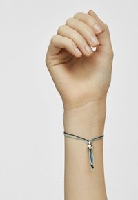 Bracciale regolabile con cordini blu e verdi caratterizzato da perline argentate, indossato su un polso umano contro uno sfondo semplice.