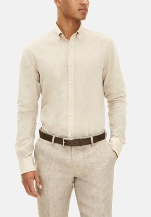 Light beige button-up shirt made of textured linen, featuring a classic collar and long sleeves, paired with tan linen trousers and a brown belt.