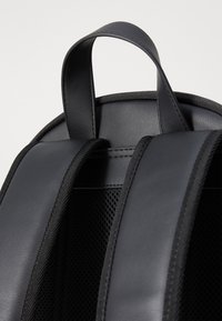 Zaino nero con un esterno in pelle liscia, dettagli in rete sul retro e spallacci imbottiti e regolabili per il massimo comfort.