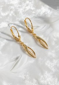 Boucles d'oreilles de couleur or avec un design en forme de feuille, ornées d'une rangée de pierres précieuses claires au centre, sur un fond doux et blanc texturé.