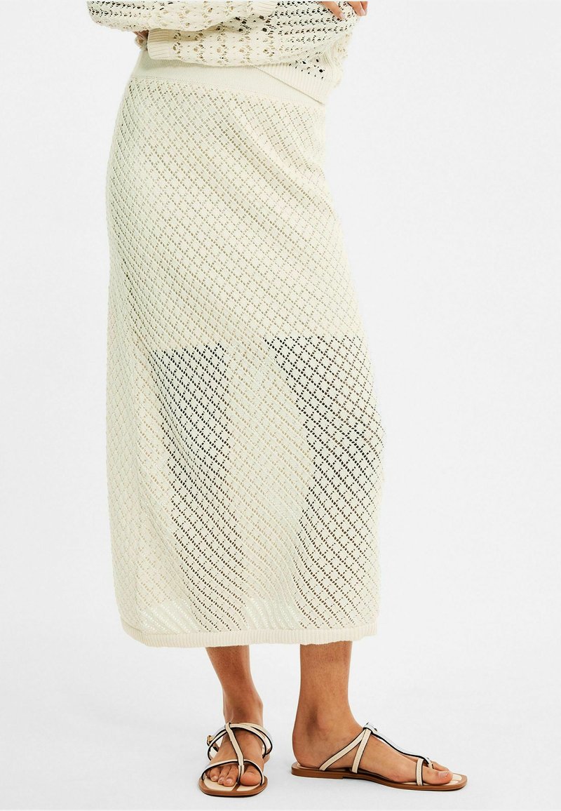 Gebreide maxi rok in crème met een open ruitpatroon en een aansluitende tailleband. Gecombineerd met platte sandalen met dunne bandjes en een gespdetail.