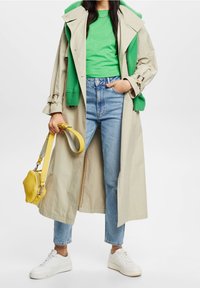 Trench coat beige, maglione verde a maglia, jeans azzurri chiari, sneakers bianche e una borsa gialla, che mostrano una varietà di trame e colori.
