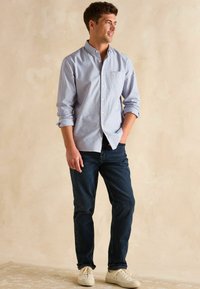 Jasnoniebieska koszula w białe paski z długim rękawem, dżinsy oraz kremowe sneakersy. Koszula ma długi rękaw i kieszonkę na piersi.