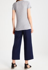 Graues Kurzarm-T-Shirt, kombiniert mit marineblauen weit geschnittenen Hosen und schwarzen Espadrilles, von hinten gesehen. Glattes, lässiges Material.