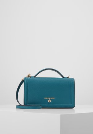 Torba Teal marki Michael Kors z uchwytem górnym oraz odpinanym paskiem na ramię na białej powierzchni ekspozycyjnej.