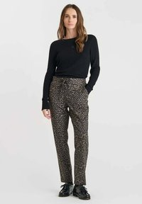 Pantalons à imprimé léopard marron et noir, dotés d'une taille à cordon de serrage et d'une coupe décontractée, associés à un haut noir à manches longues et côtelé.