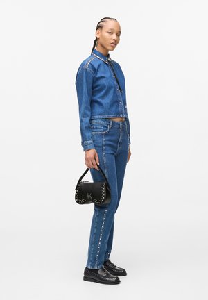 Denimska krajša jakna s kovinskimi aplikacijami, v kombinaciji z ujemajočimi se oprijetimi skinny hlačami. Črna torbica z žebljičkastimi detajli in kratko ročico. Črne čevlje.