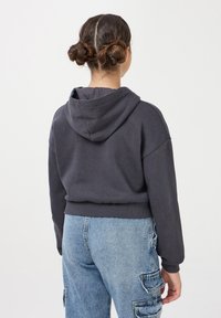 Ciemnoszara, krótkia bluza z kapturem, wykonana z miękkiego materiału, z ribbowanym dołem. Noszona z jasnoniebieskimi spodniami cargo z kieszeniami.