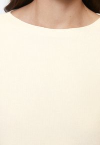 Pull couleur crème avec une texture côtelée, encolure ronde et tissu lisse. Vue en gros plan montrant les détails du motif tricoté.