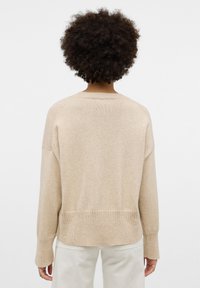 Maglione beige lavorato a maglia con vestibilità rilassata, polsini e orlo a costine, caratterizzato da un colletto rotondo e spalle scese. Texture morbida.