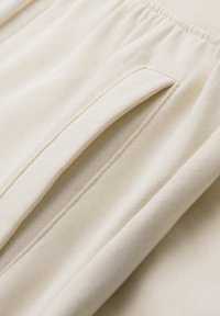 Close-up af beige stofbukser, der viser en elastisk linning og en lodret sidelomme med en syning ved åbningen.