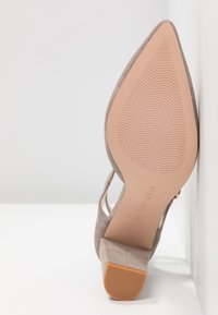 Chaussure à talons hauts en daim gris avec un bout pointu et des côtés découpés. Caractéristiques : semelle en caoutchouc texturé et talon carré.