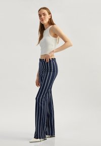 Marineblauwe gestreepte flared broek met een hoge taille, gemaakt van textuurstof, gecombineerd met een nauwsluitende witte tanktop en puntige witte schoenen.