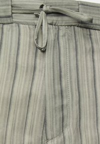 Pantaloni a righe realizzati in un tessuto leggero, con vita regolabile, una sottile texture e tonalità di grigio che variano, accompagnate da righe di grigio scuro.