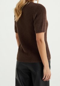 Brun stickad tröja med korta ärmar och en texturerad yta, tillsammans med svarta läderbyxor. Tröjan har en avslappnad passform och rundad hals.