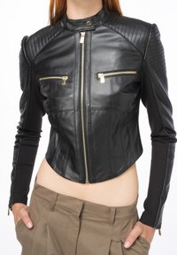 Černá zkrácená bunda z kůže s prošívanými rameny, která má dvě přední zipové kapsy a zlaté kovové akcenty. Hladká textura.