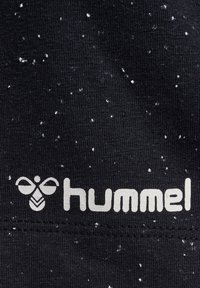Svart tyg med en strukturerad yta, med vita prickar och en tryckt logotyp "hummel" i ljusgrått.