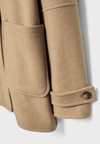 Manica di un cappotto di lana beige con una grande tasca rettangolare e un dettaglio a strap con bottone vicino al polsino.