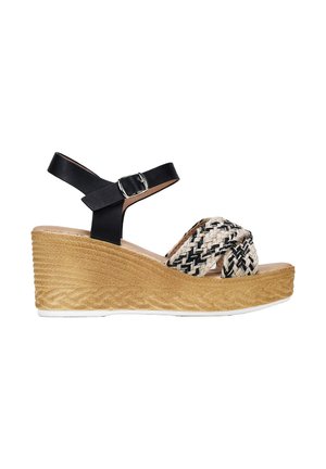 Sandalia de cuña con parte superior tejida en negro y beige y tirante negro en el tobillo. Presenta una plataforma texturizada en beige y suela blanca.